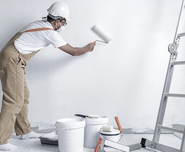 Painter Applying White Paint Next to Ladder and Paint Buckets