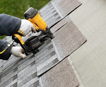 Worker Installing Shingles on Roof with Nail Gun